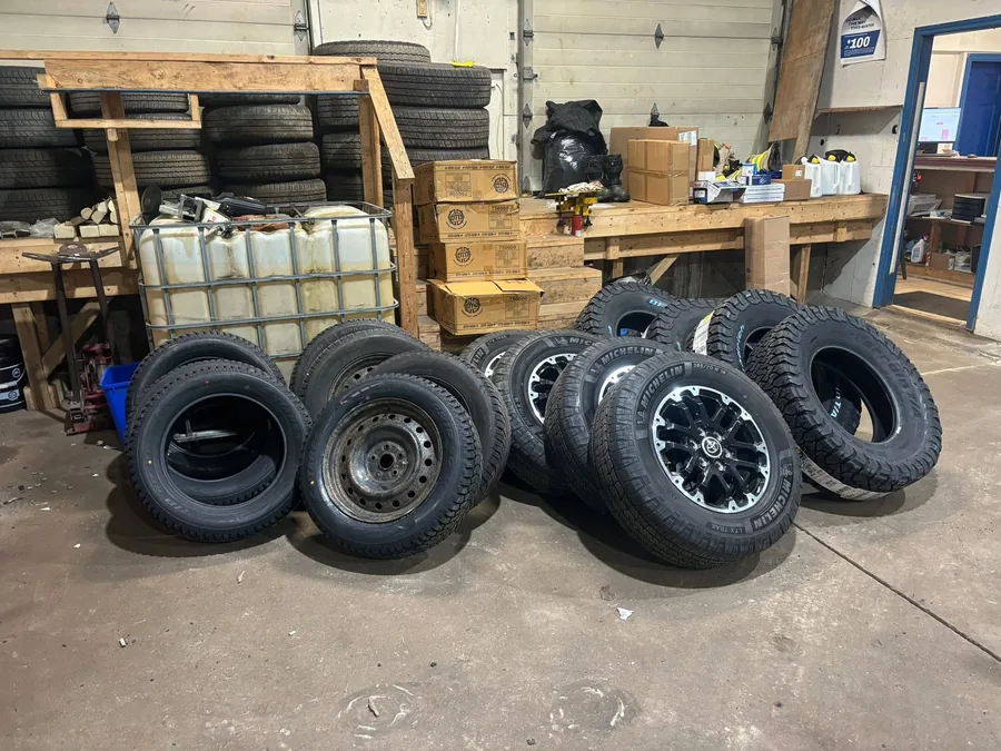 Customer tire sets on steel and alloy rims standing on the shop floor at AutoNorth Auto Repair in North Bay, with more tires racked on wooden shelving behind them