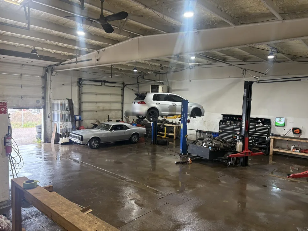 A white SUV raised on a hoist and an older white muscle car in the next bay inside AutoNorth Auto Repair in North Bay
