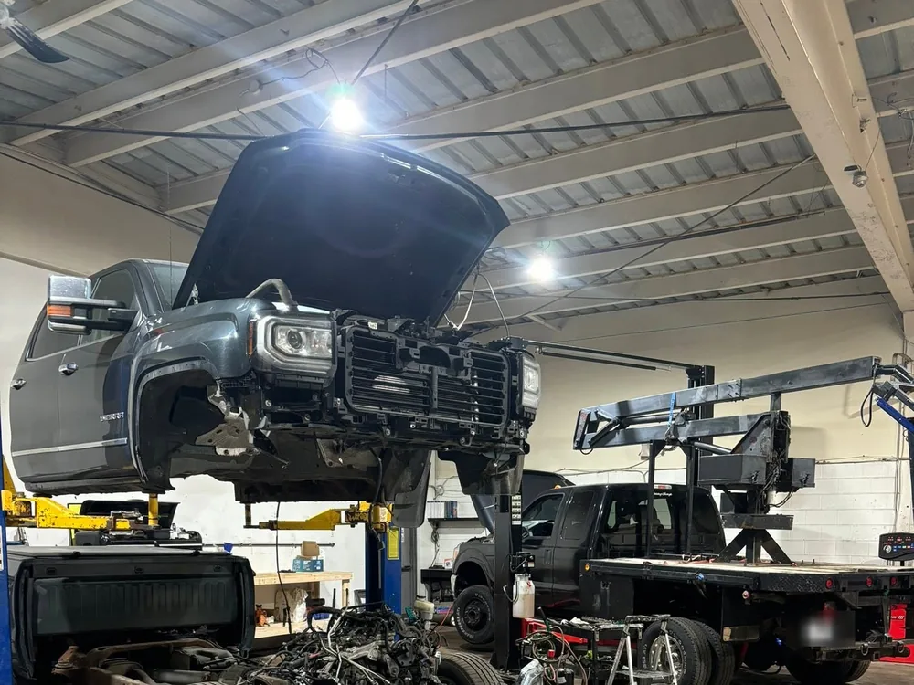 Grey GMC pickup raised on a two-post hoist inside AutoNorth Auto Repair with its hood up and the front bumper and grille assembly removed