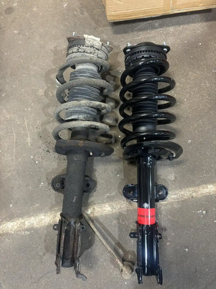 Two strut assemblies side by side on the shop floor, one corroded with a bare metal spring and one clean with a black-coated spring