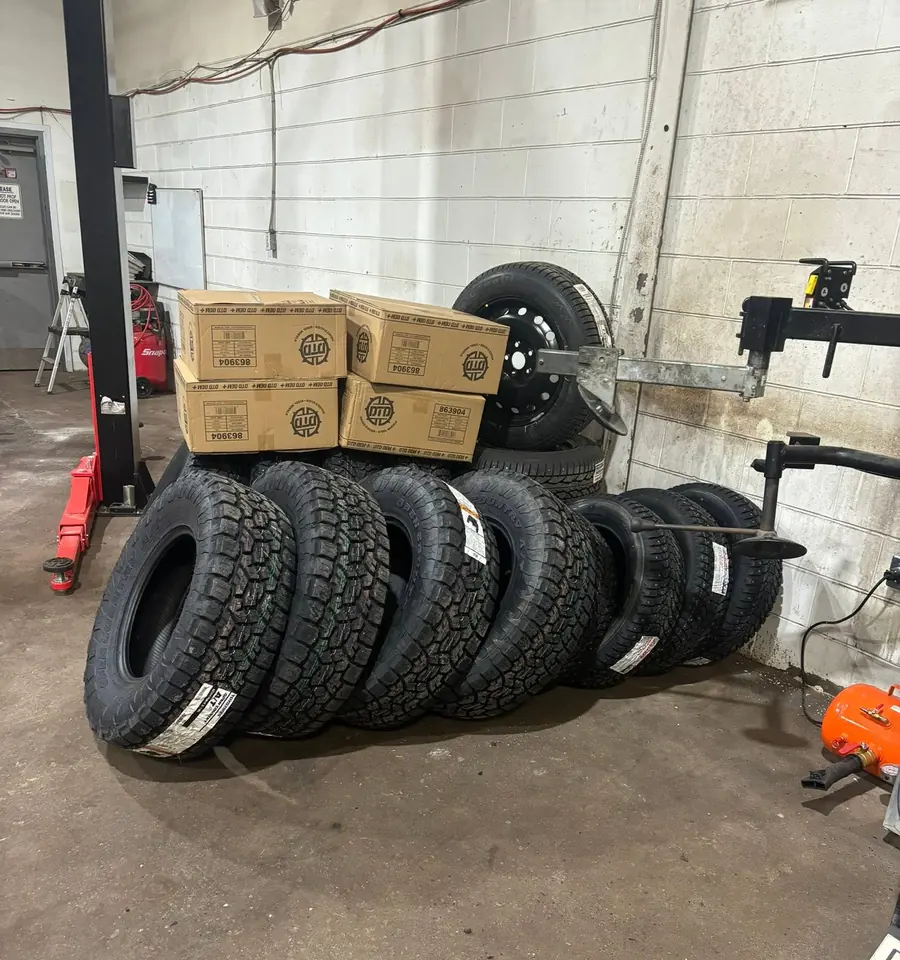 A row of tires standing against the wall at AutoNorth Auto Repair in North Bay, one mounted on a black steel wheel, with stacked parts boxes and a tire machine arm behind them