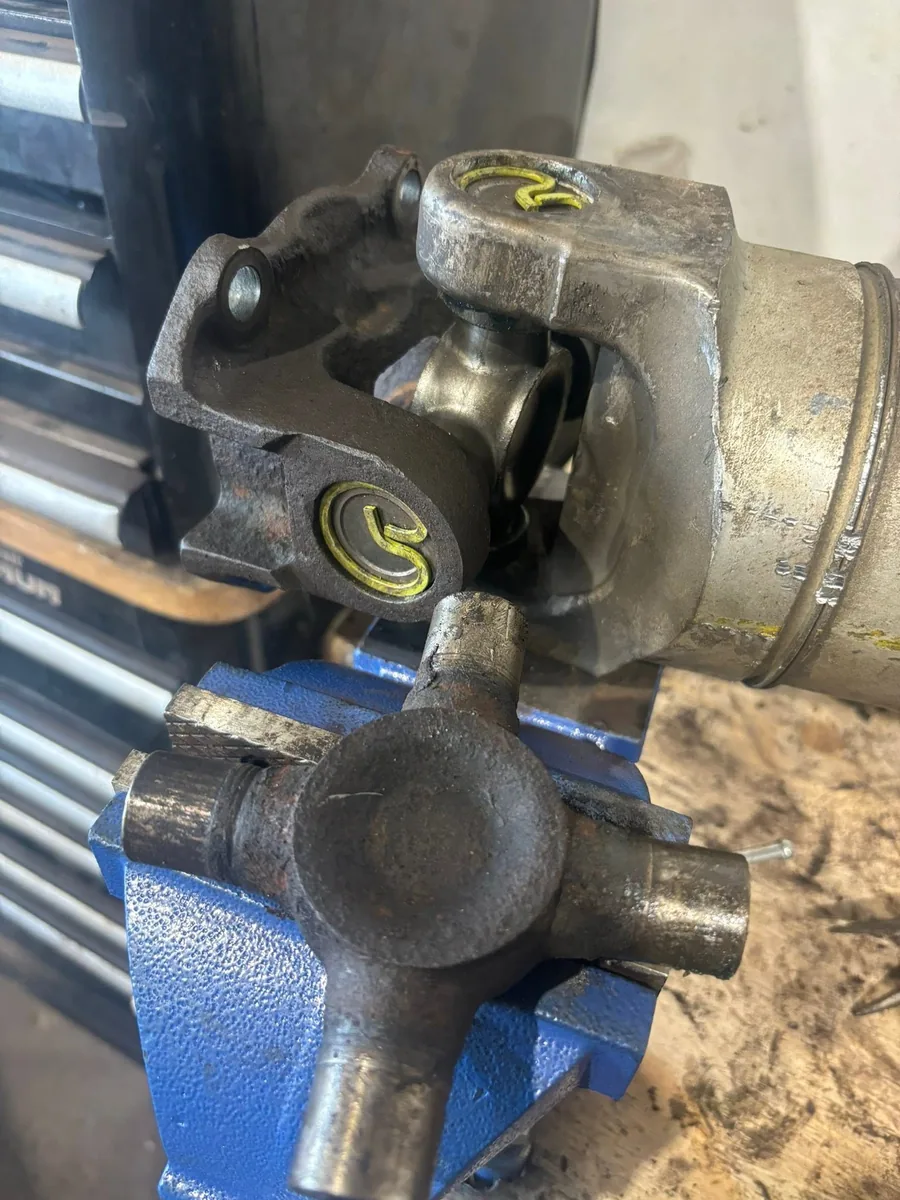 Driveshaft yoke and universal joint clamped in a blue bench vise at AutoNorth, with a worn u-joint cross held in the jaws below it